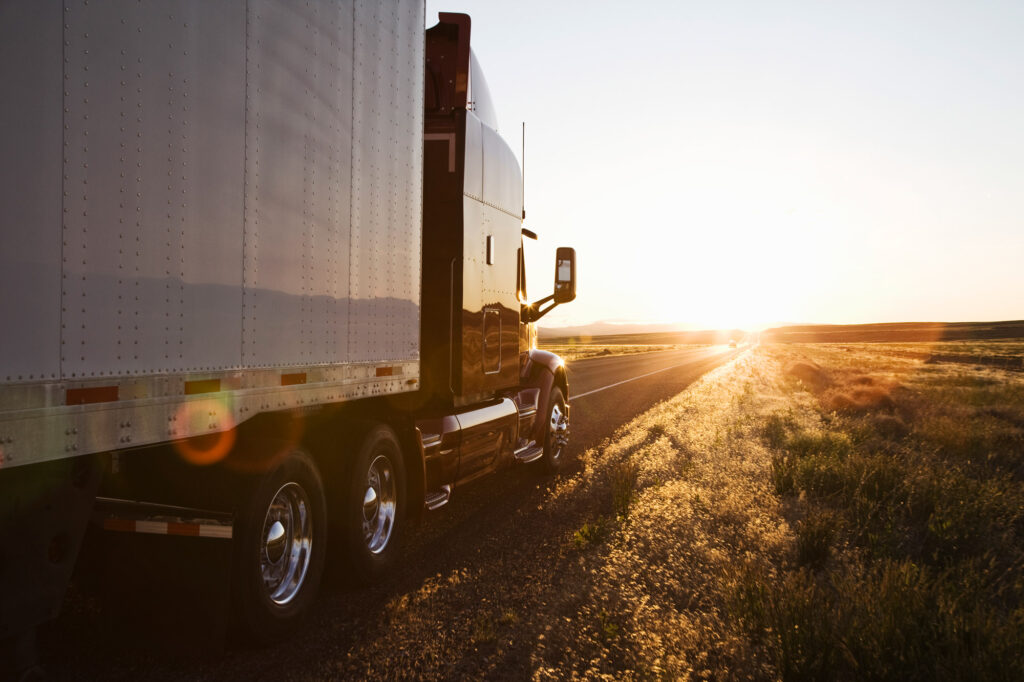 Side view of a trailer and truck on the side of the road at sunset