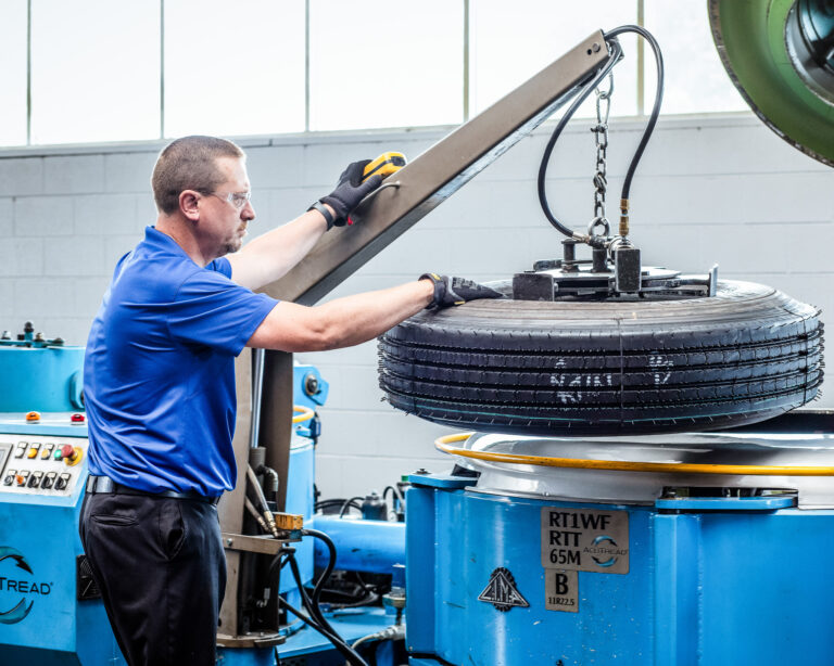 AcuTread technician lifting a newly retreaded tire from a mold curing press