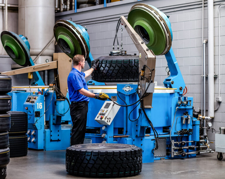 AcuTread technician lifting a large newly retreaded tire from a mold curing press